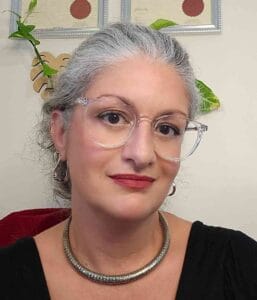 Portrait of a mature woman with glasses and silver hair in an office setting.