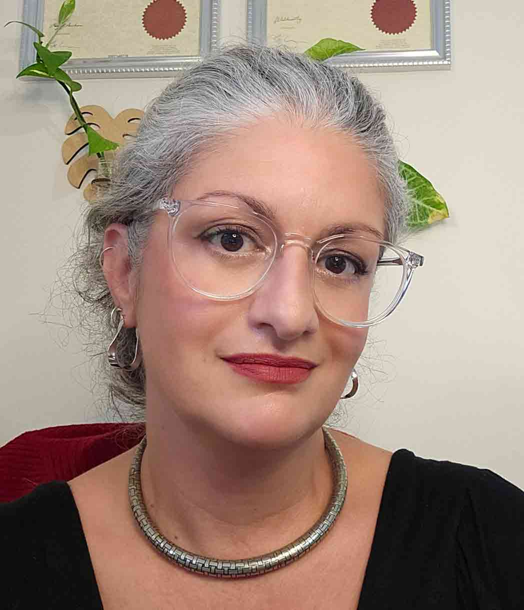 Portrait of a mature woman with glasses and silver hair in an office setting.