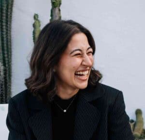 Equana Minds professional woman smiling with dark hair and black blazer in a modern office.