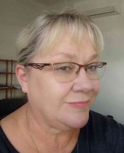 Portrait of a woman with short blonde hair and glasses, smiling softly.
