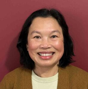Smiling woman with shoulder-length black hair against a red background, representing Equana Minds.