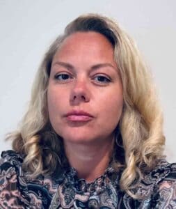 Portrait of a woman with blonde curly hair and a patterned blouse, representing Equana Minds.