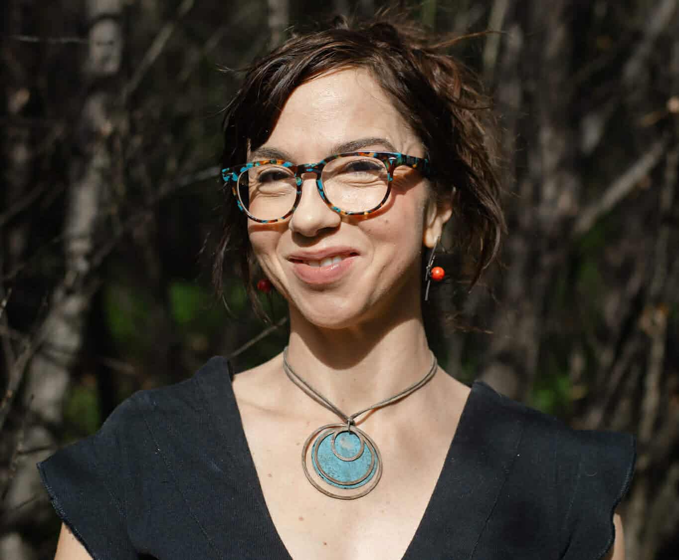 Portrait of a woman with short dark hair and glasses outdoors, smiling.