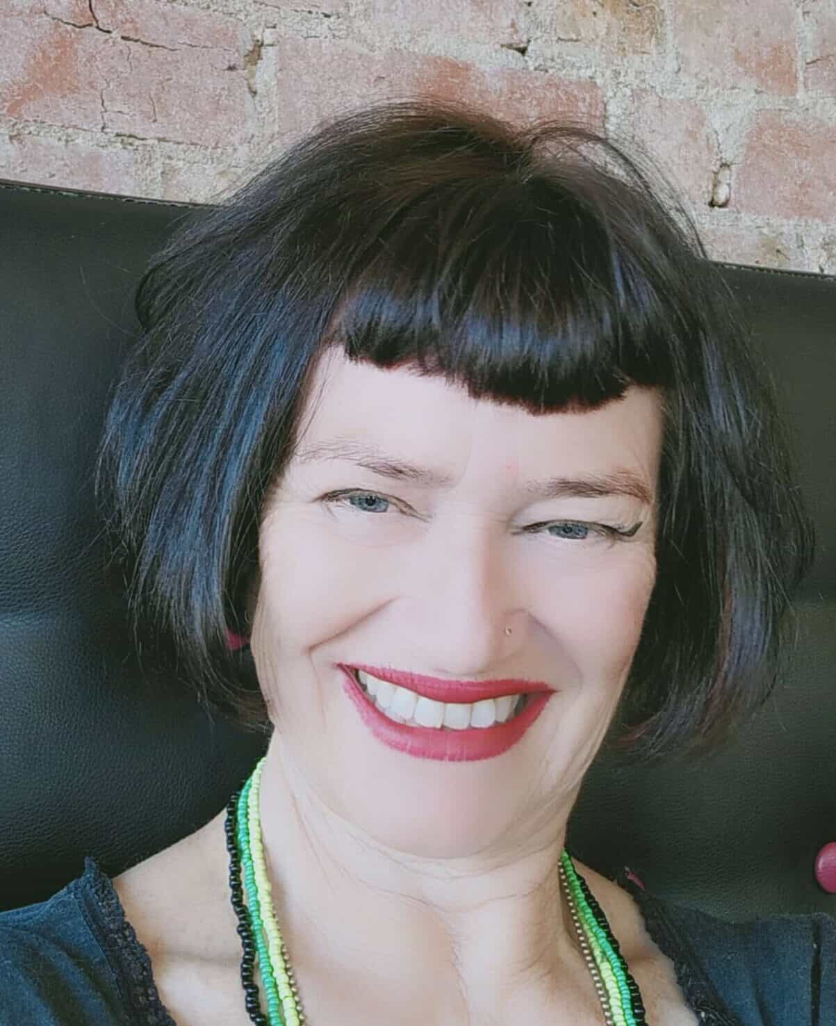 Smiling woman with short black hair and red lipstick in front of brick wall.