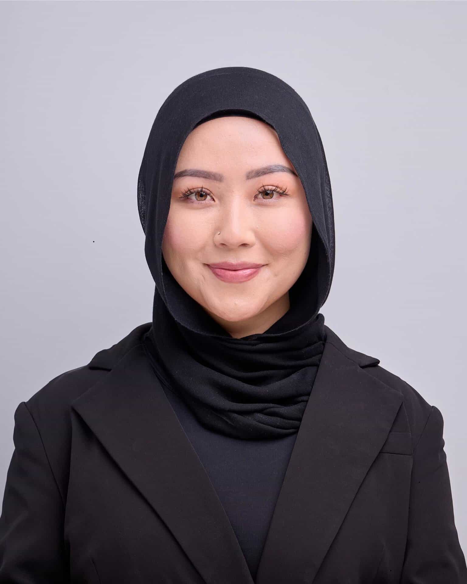Professional woman wearing a black hijab and blazer smiling at the camera.