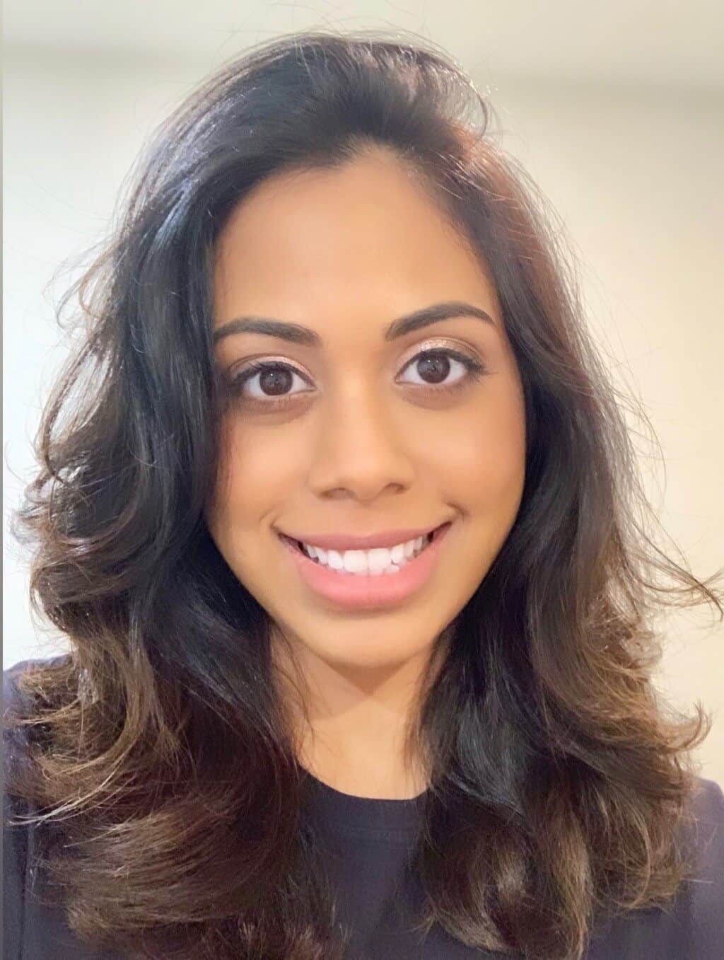 Smiling woman with wavy dark hair and natural makeup in a professional setting.