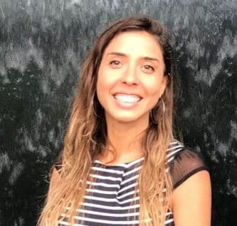 Smiling woman with long wavy hair in front of a dark textured background.