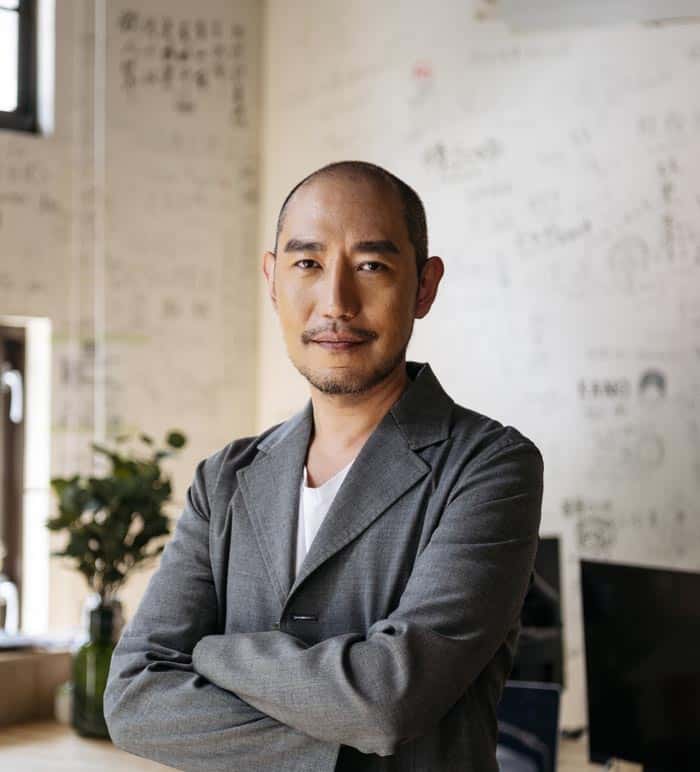 Confident professional man in a grey suit in an office setting with whiteboard and plants.